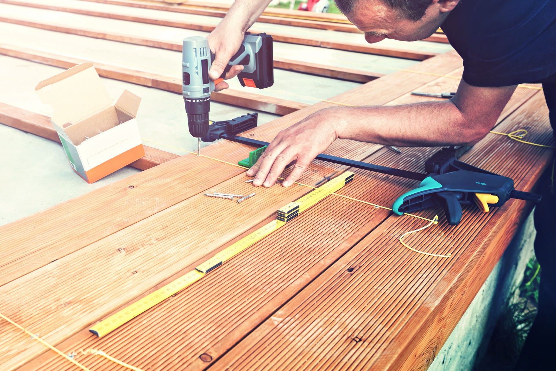 Construction worker screwing down wood deck with battery power screw gun or drill.